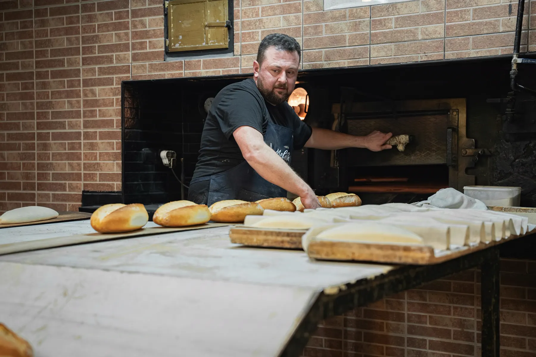 Bäcker holt frische Brotlaibe aus dem Steinofen
